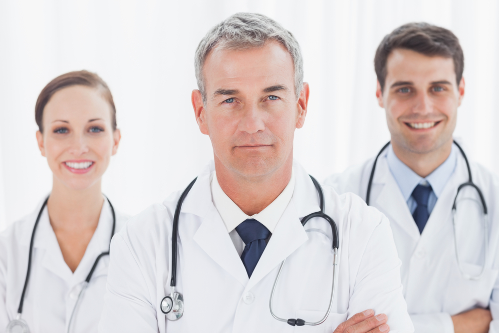 Cheerful doctors posing together crossing arms in bright office